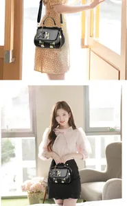 Close-up of black handbag featuring white daisy embroidery and golden H-shaped metal buckle