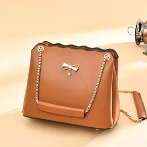 Brown crossbody bag with gold bow detail and chain strap on a warm neutral background