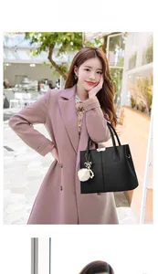 Sac à main noir à motif litchi avec pompon blanc et breloque perle porté par un mannequin