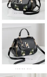 Close-up of black embroidered handbag with H-shaped gold buckle and pearl floral charm