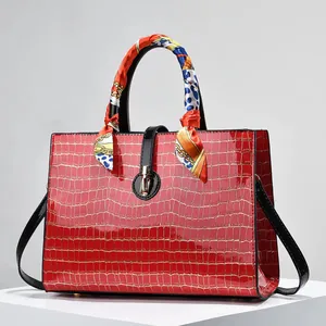 Detailed macro view of red crocodile-embossed handbag with silk scarf on handle and gold lock