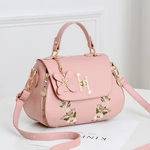 Pink PU crossbody bag with white flower embroidery and pearl clasp on white background