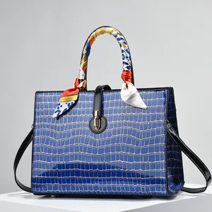 Blue crocodile embossed handbag with black handles and patterned silk scarf detail