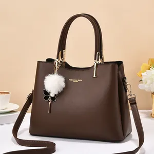 Detail of dark brown leather tote bag with gold hardware and plush pompom charm