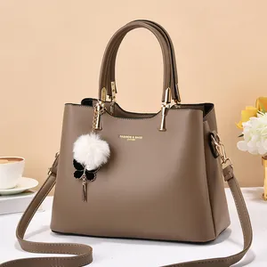 Brown leather handbag with large capacity and pom-pom charm, shown in a lifestyle setting