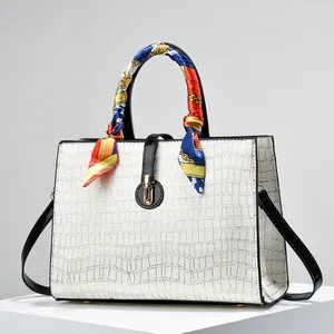 Detail of embossed crocodile pattern on white leather bag with decorative silk scarf handle