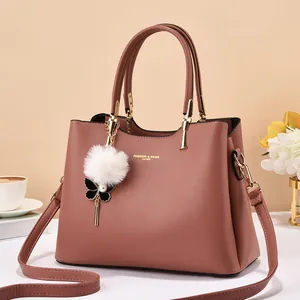 Close-up of pink leather handbag featuring gold hardware and a fluffy pom-pom charm