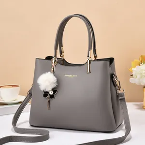 Detail of grey leather tote bag featuring gold lettering and a stylish plush charm