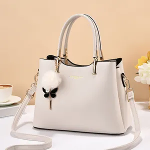 Close-up of cream handbag with gold lettering and plush pompom butterfly charm