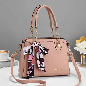 Detailed close-up of a pink pebbled leather handbag with chain handle and floral scarf