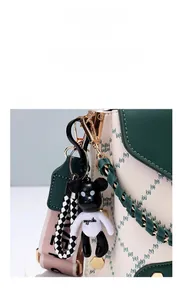 Detail of cartoon bear pendant on a green crossbody bag with woven wrist strap
