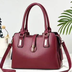 Dettaglio macro della borsa rosso vino con hardware dorato e profilo a trapezio elegante