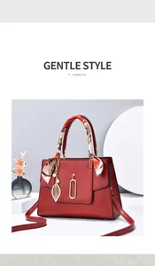 Detail of red pebbled leather handbag with decorative silk scarf and metal leaf pendant