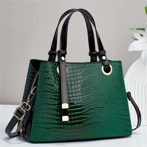 Detail view of dark green crocodile embossed handbag with sleek black handles and gold hardware