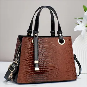 Close-up of brown crocodile pattern handbag with glossy black straps and gold hardware