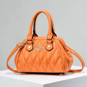 Detalle de bolso acolchado naranja con cierre dorado de corazón y asa superior elegante