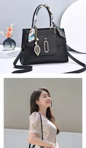 Detail of black pebbled leather handbag with silk scarf handle and gold leaf charm
