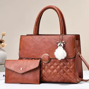 Detail of brown quilted faux leather tote set with gold fastener and white pompom charm