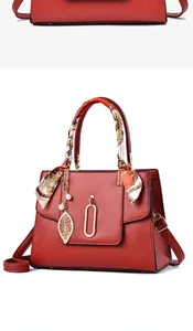Detail view of red leather handbag featuring silk scarf handle and golden leaf pendant