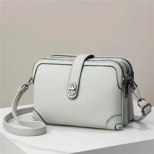 Detail view of light grey pebble leather crossbody bag with three zipper compartments