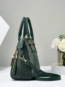 Detail of dark green crocodile embossed handbag with gold cat charm and side zipper