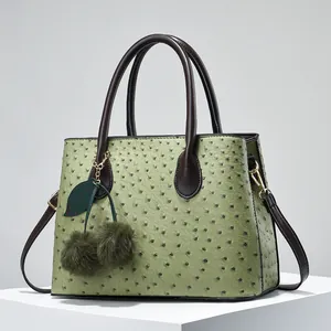 Detail of ostrich-textured green tote bag with cherry pompom charm and gold hardware