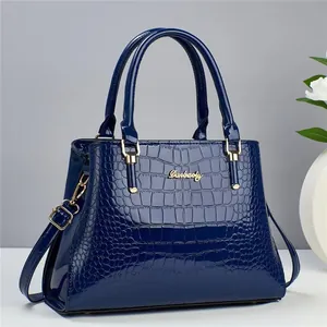 Close-up of deep blue crocodile-embossed patent leather handbag with gold metal logo