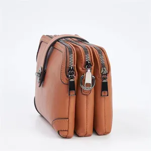 Detail view of the brown leather texture and three separate zipper compartments of the bag