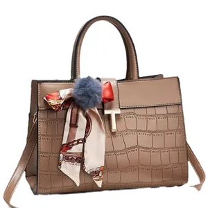 Sac à main kaki motif crocodile avec foulard en soie et pompon sur fond blanc