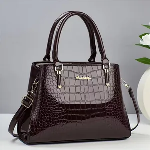 Close-up of dark burgundy crocodile-patterned handbag with golden brand plate and shiny finish