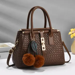 Brown woven texture handbag with dual handles, gold hardware, and furry pompom charm