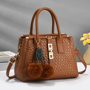 Detail of brown woven texture handbag with cherry-shaped fur pompom and golden hardware