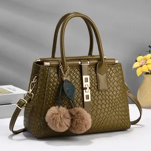 Close-up of olive green woven leather bag with gold buckle and cherry fur ball charms