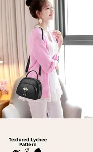 Détail d'un sac bandoulière noir avec motif litchi et pendentif cygne porté par un modèle