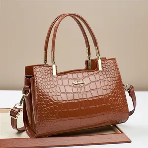 Detailed view of crocodile embossed leather texture and gold logo on brown tote bag