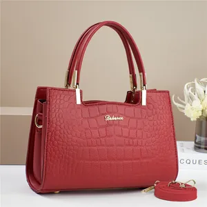 Detail of red crocodile pattern handbag with gold logo, metal feet, and strap