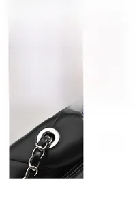Detail of silver chain strap and metal eyelets on a black quilted crossbody bag
