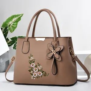 Close-up of brown faux leather handbag featuring elegant floral embroidery and butterfly charm