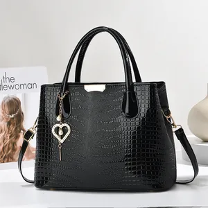 Gros plan du sac à main noir motif crocodile avec pendentif cœur doré et perle