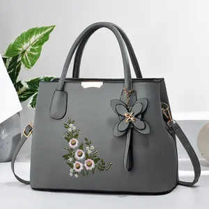 Detail of grey leather tote bag featuring elegant floral embroidery and golden metal accents