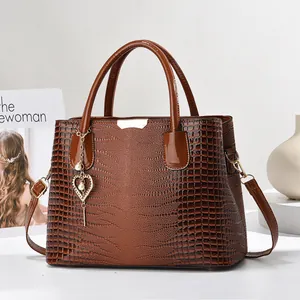Détail de la texture crocodile marron foncé et du pendentif cœur perlé sur le sac à main