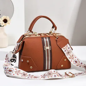Détail macro du sac en cuir marron avec bandoulière fleurie et ornement de papillon