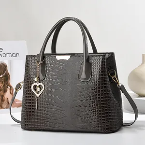 Détail de la texture crocodile et du pendentif perle cœur sur un sac à main marron