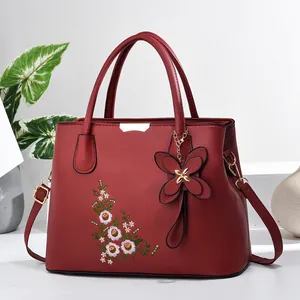 Detailed close-up of dark red handbag with floral embroidery and butterfly pendant