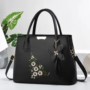 Detail of floral embroidery and butterfly charm on black textured leather handbag