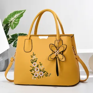 Close-up of yellow handbag featuring elegant floral embroidery and butterfly pendant