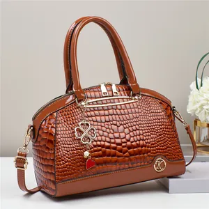 Close-up of brown crocodile embossed handbag with golden K logo and floral accessories