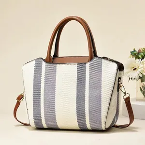Close-up of contrast striped canvas bag featuring brown leather handles and metal hardware
