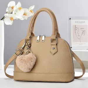 Detail of khaki shell handbag with lychee texture and plush heart charm on a display stand