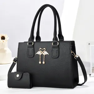 Detalle del set de bolso tote en cuero negro con colgante de cisne dorado y billetera